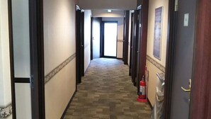 A hotel hallway with carpeted floors, doors on both sides, and a fire extinguisher on the right.