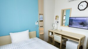 A hotel room with a bed, a desk with a chair, a small refrigerator, a mirror, a clock, and a TV on the wall.