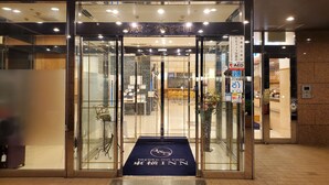 L’entrée d’un hôtel avec une porte en verre, un tapis bleu orné du nom de l’hôtel et un panneau indiquant la présence d’un distributeur automatique de billets.