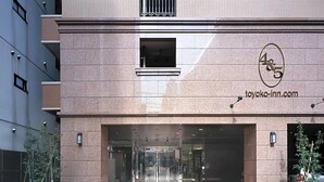 L’entrée d’un hôtel, avec une porte en verre, une enseigne portant le logo et l’adresse du site web, et un chemin dallé menant à l’entrée.