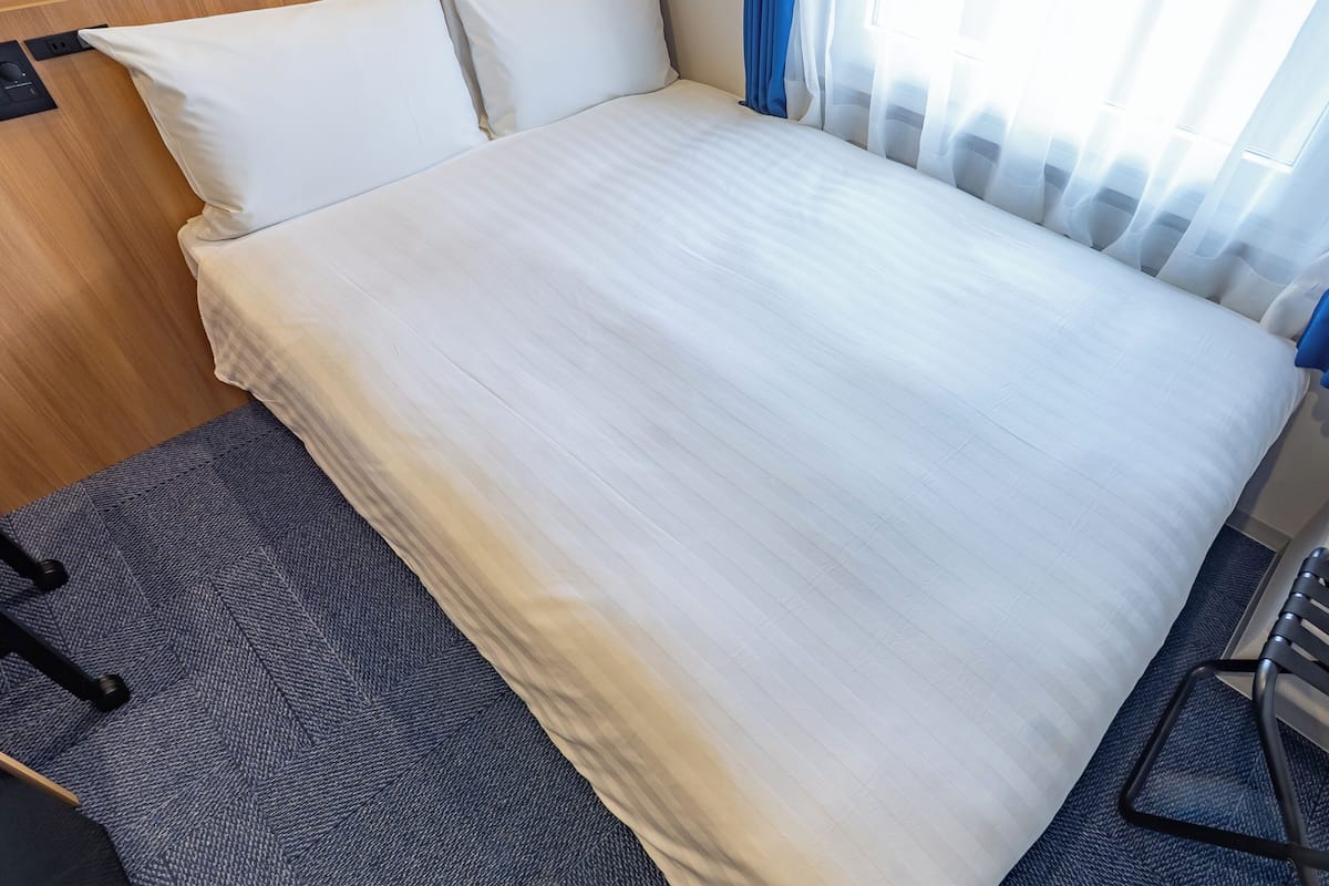 A neatly made bed with white linens, a wooden headboard, and a blue carpeted floor.