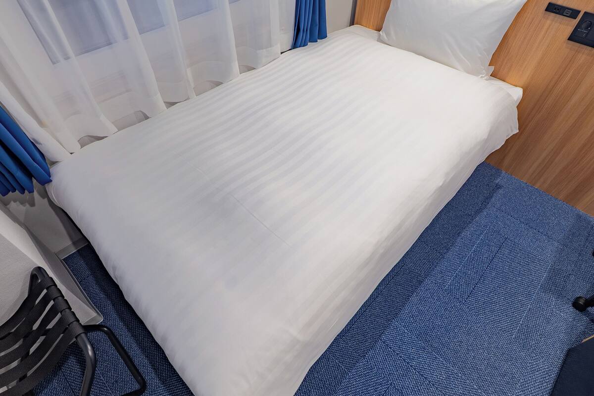 A neatly made bed with white linens, a wooden headboard, and a blue textured rug.