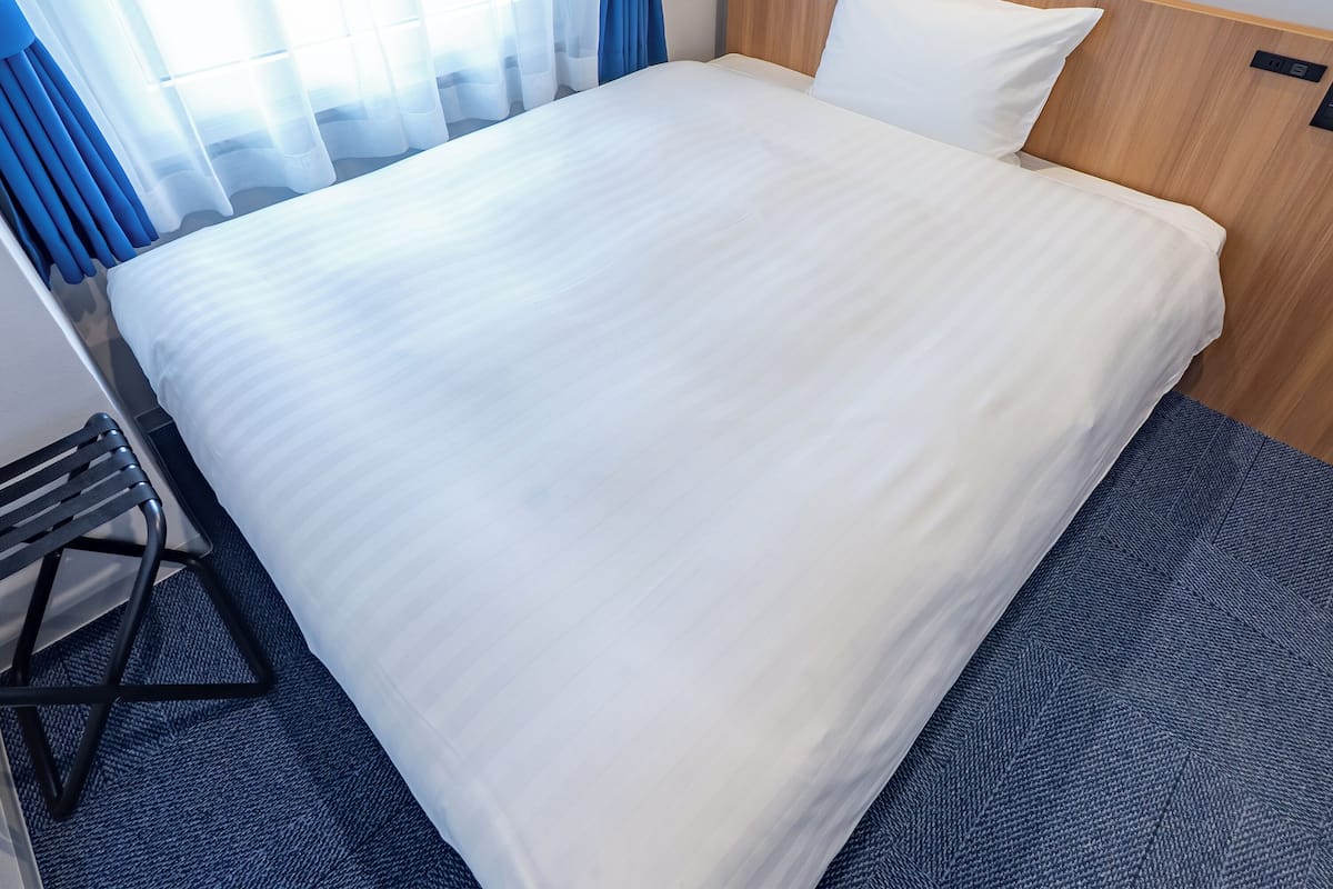 A neatly made bed with white linens in a hotel room.