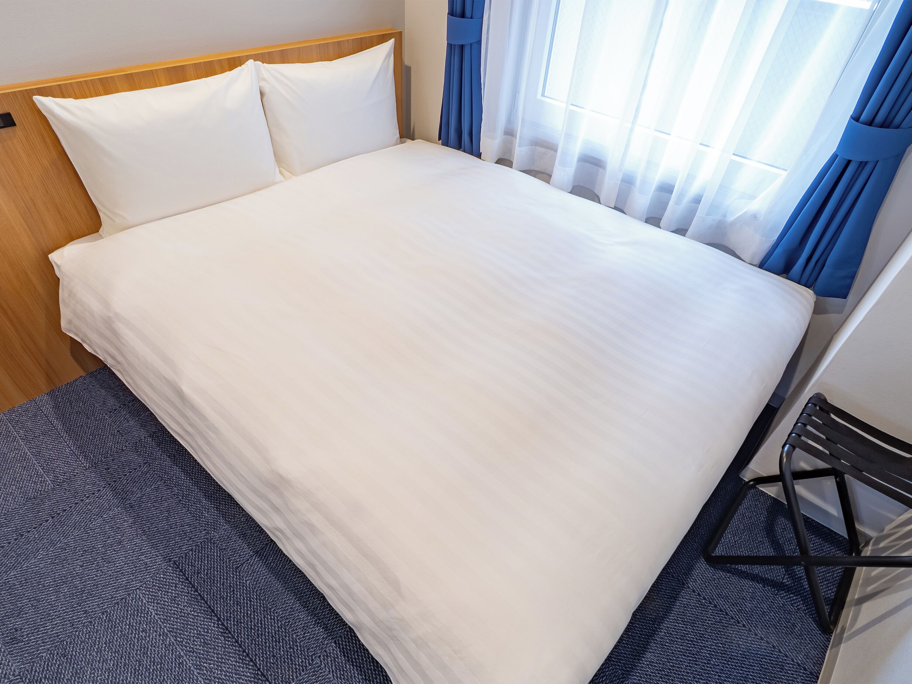 Una habitación de hotel con una cama grande, cabecera de madera y alfombra azul.