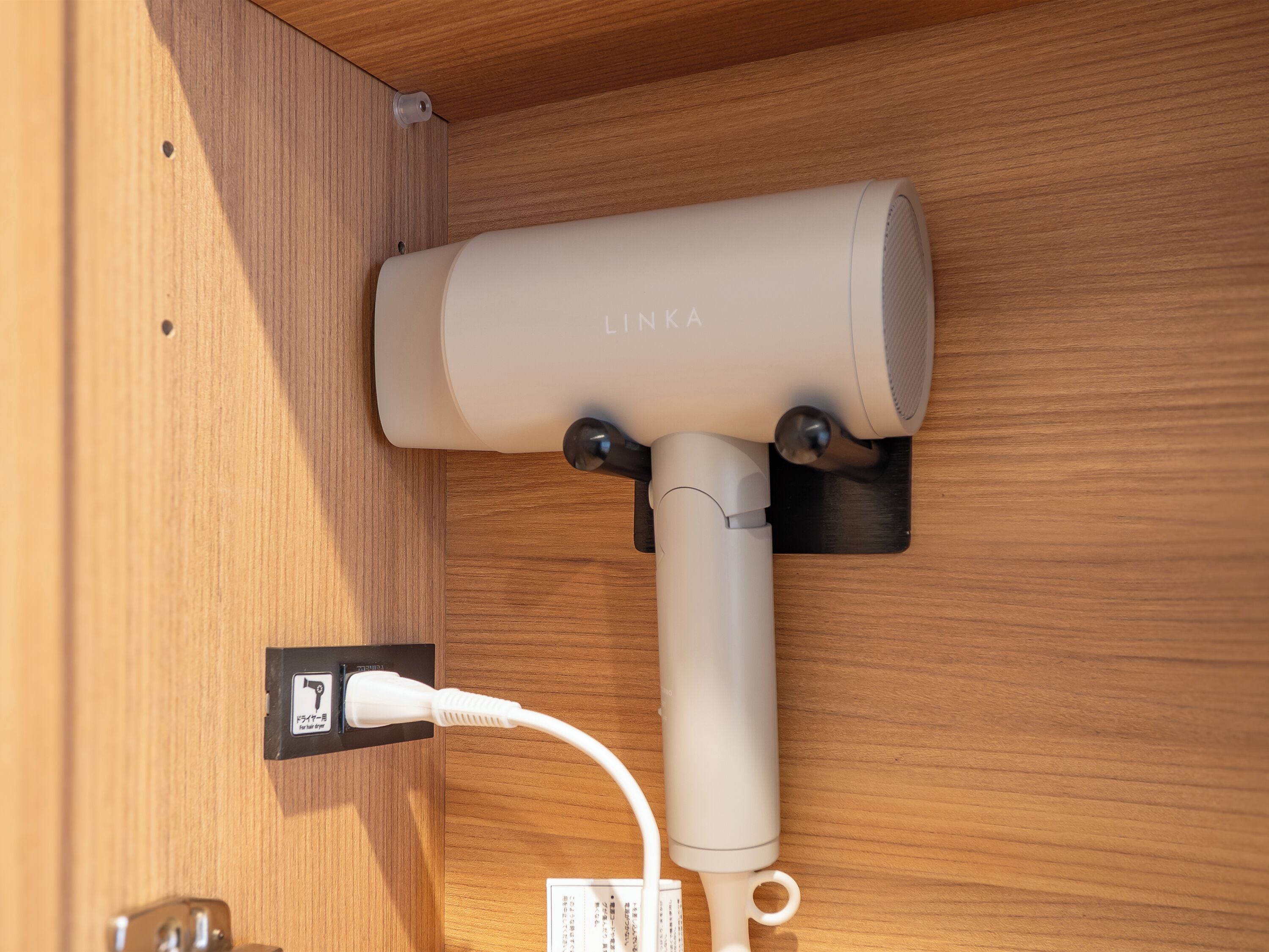 Un purificador de aire blanco portátil con la marca LINKA, enchufado a un enchufe de pared sobre una superficie de madera.