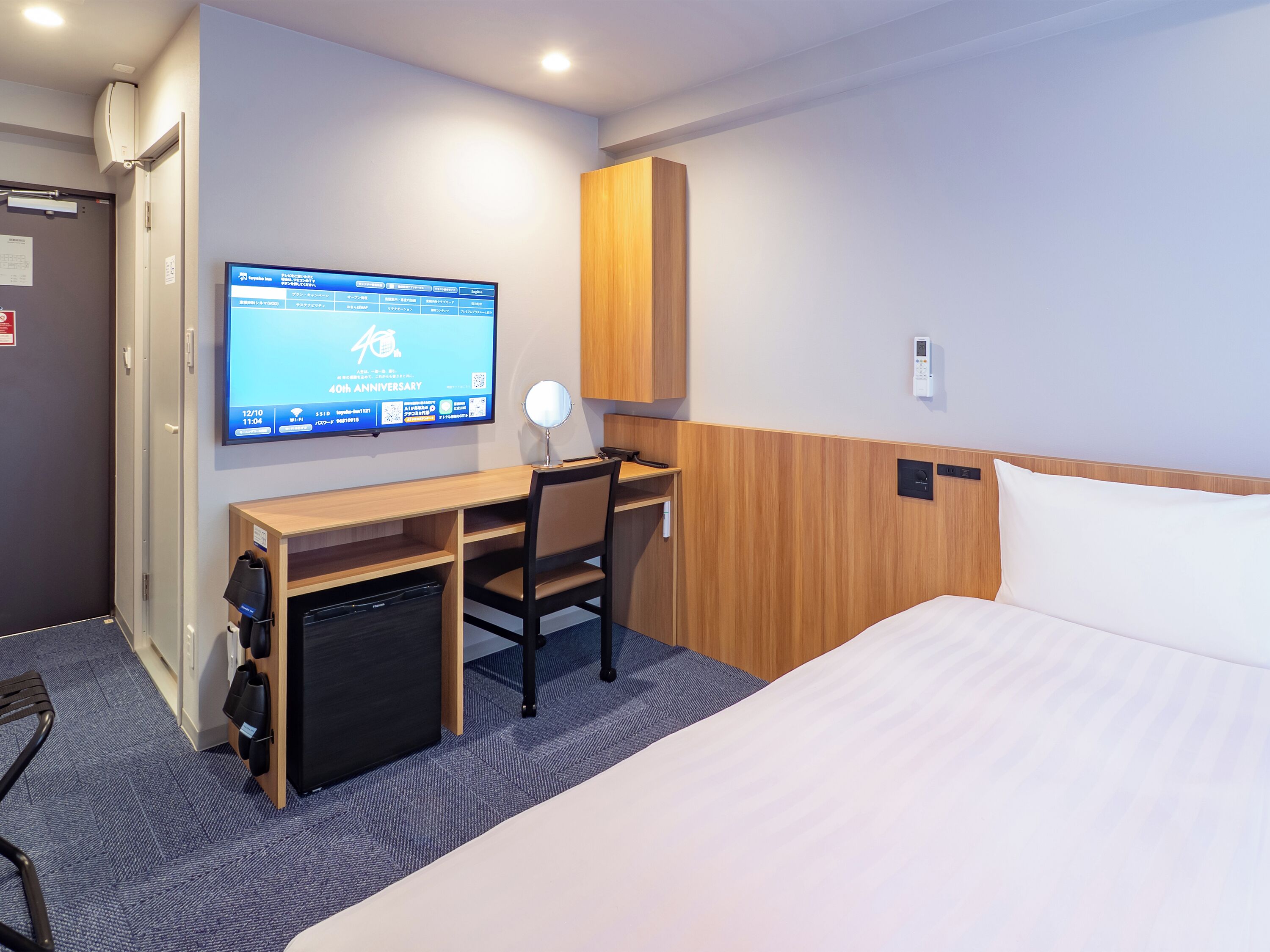 Una habitación de hotel con cama, escritorio, silla, televisor y minibar.