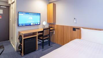 Una habitación de hotel con cama, escritorio, silla, televisor y minibar.