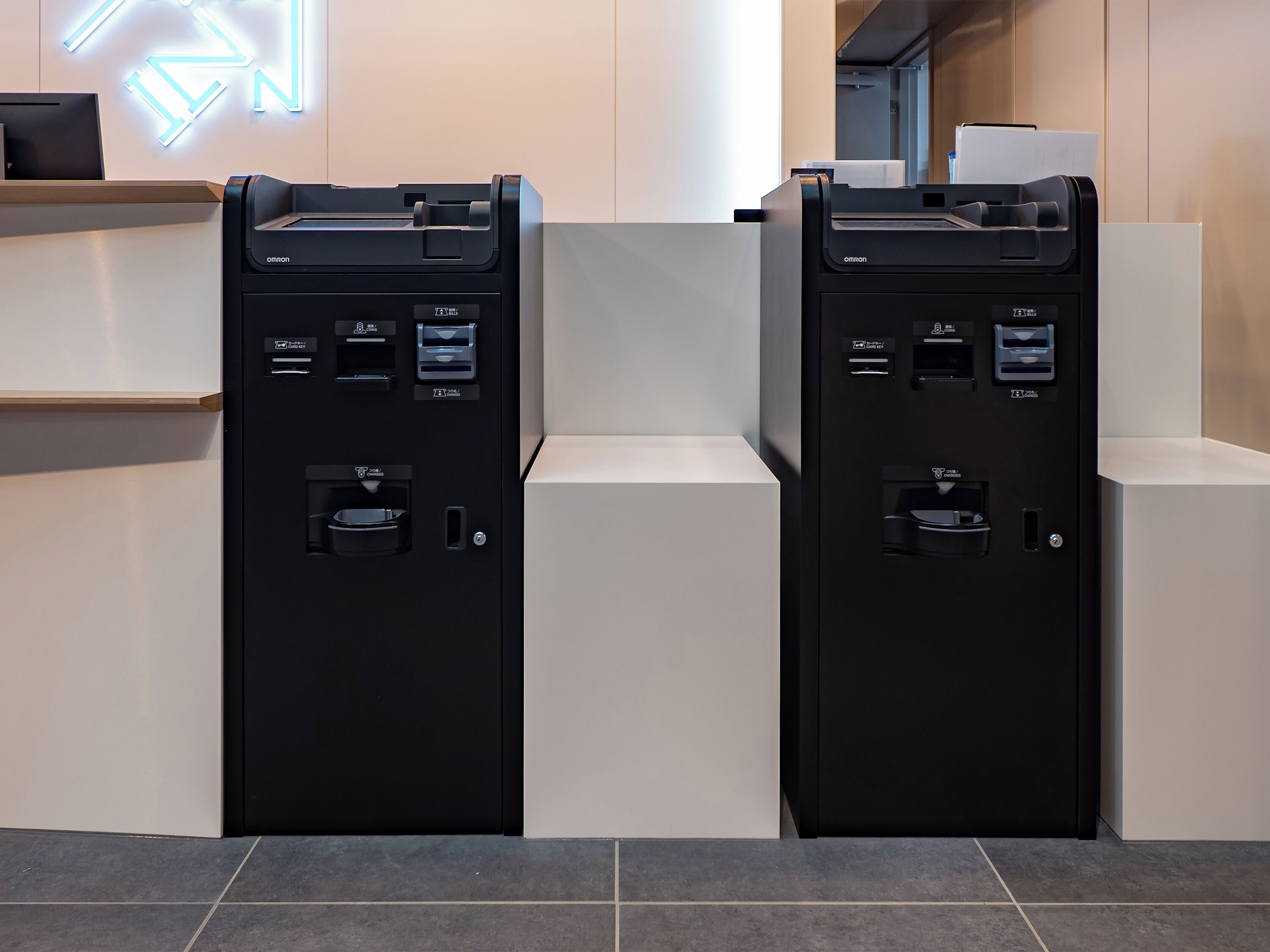 Two black self-service kiosks with card readers, a cash dispenser, and a paper dispenser.