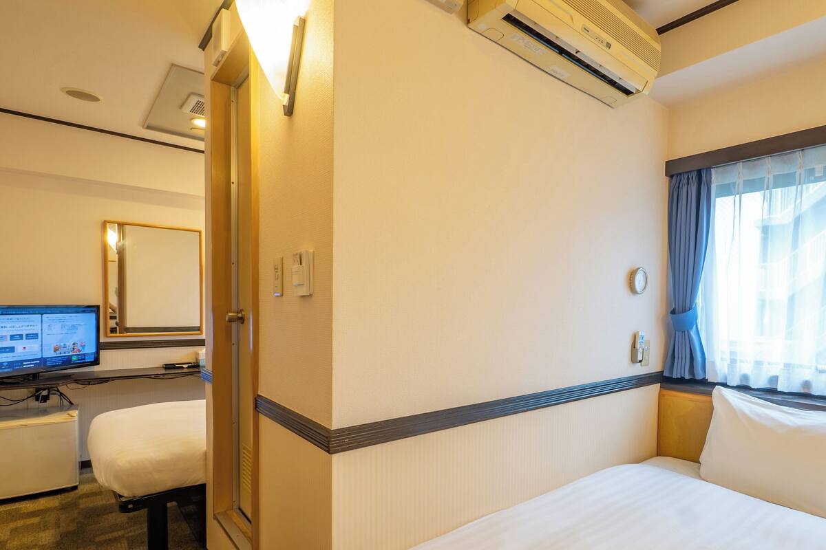 Een hotelkamer met een bed, een bureau met een computer, een spiegel en een airconditioning.