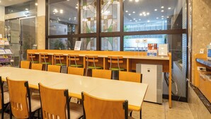 Un espace repas comprenant une longue table, plusieurs chaises, un réfrigérateur et une fenêtre donnant sur l’extérieur.