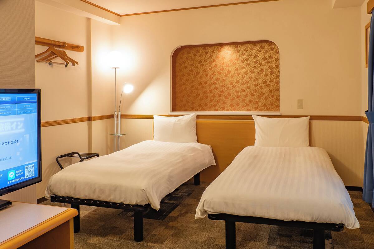 Een hotelkamer met twee enkele bedden, een bureau met een computer, een staande lamp en een klok aan de muur.