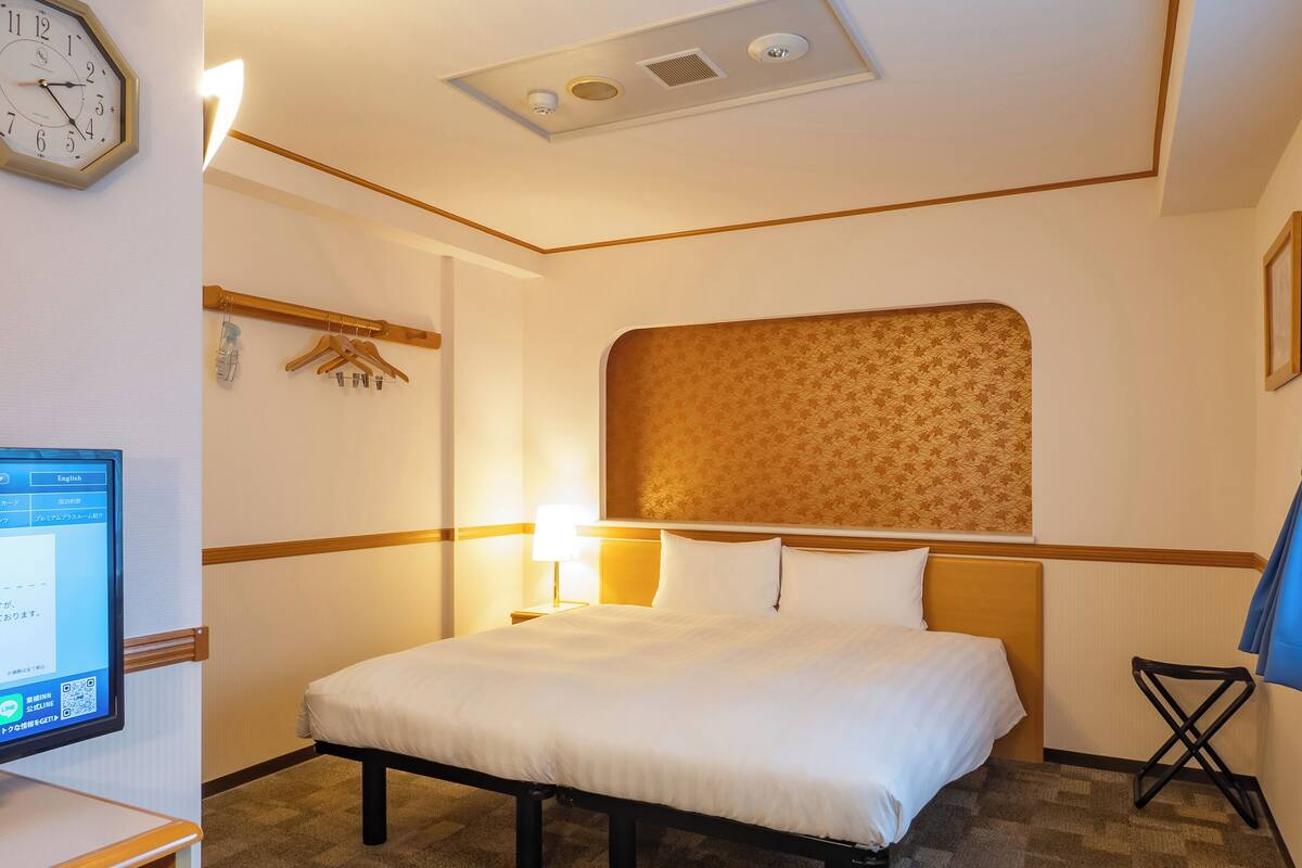 Een hotelkamer met een bed, nachtkastje, lamp en een klok aan de muur.