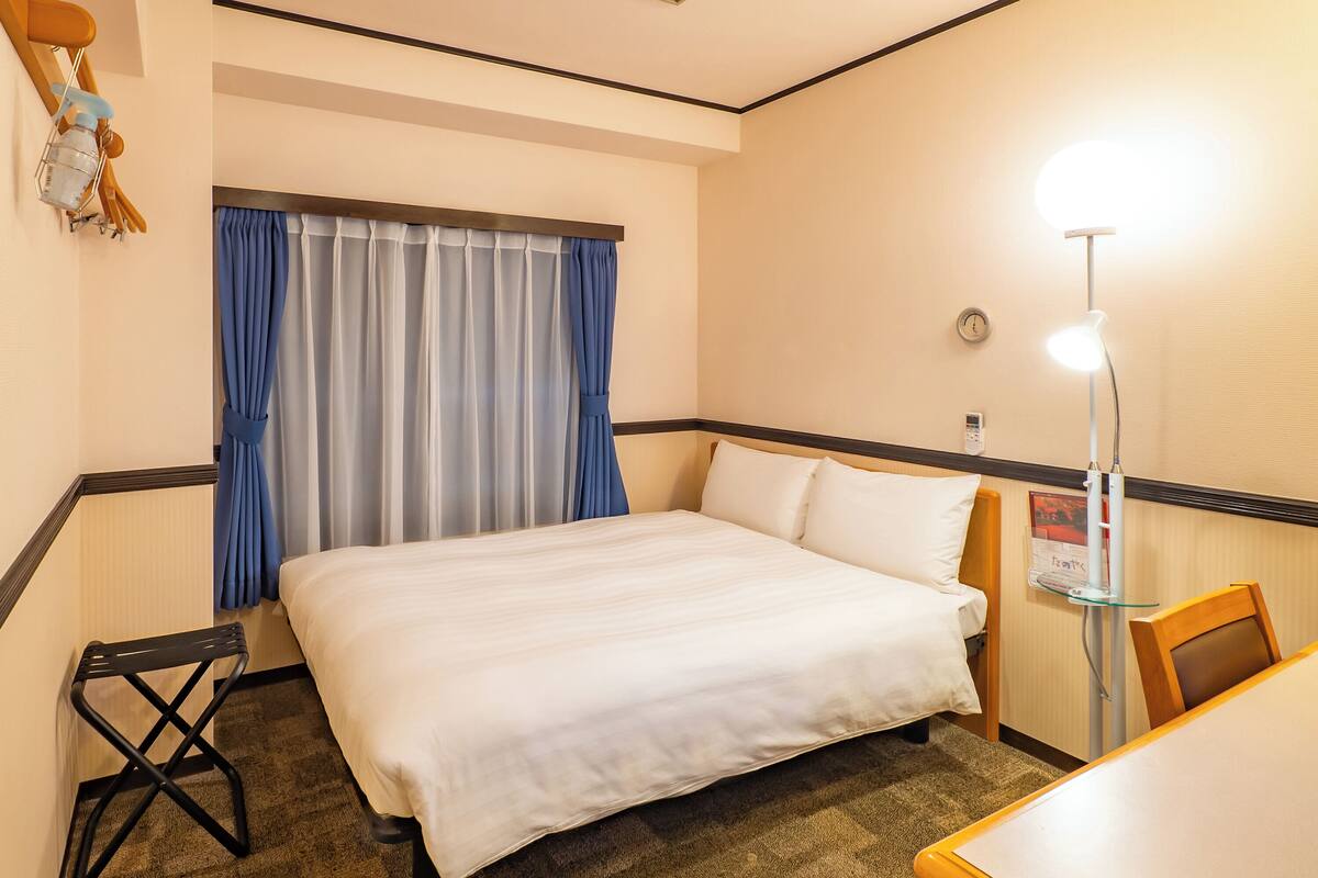 Hotelkamer met een bed, bureau, stoel, lamp en raam met gordijnen.