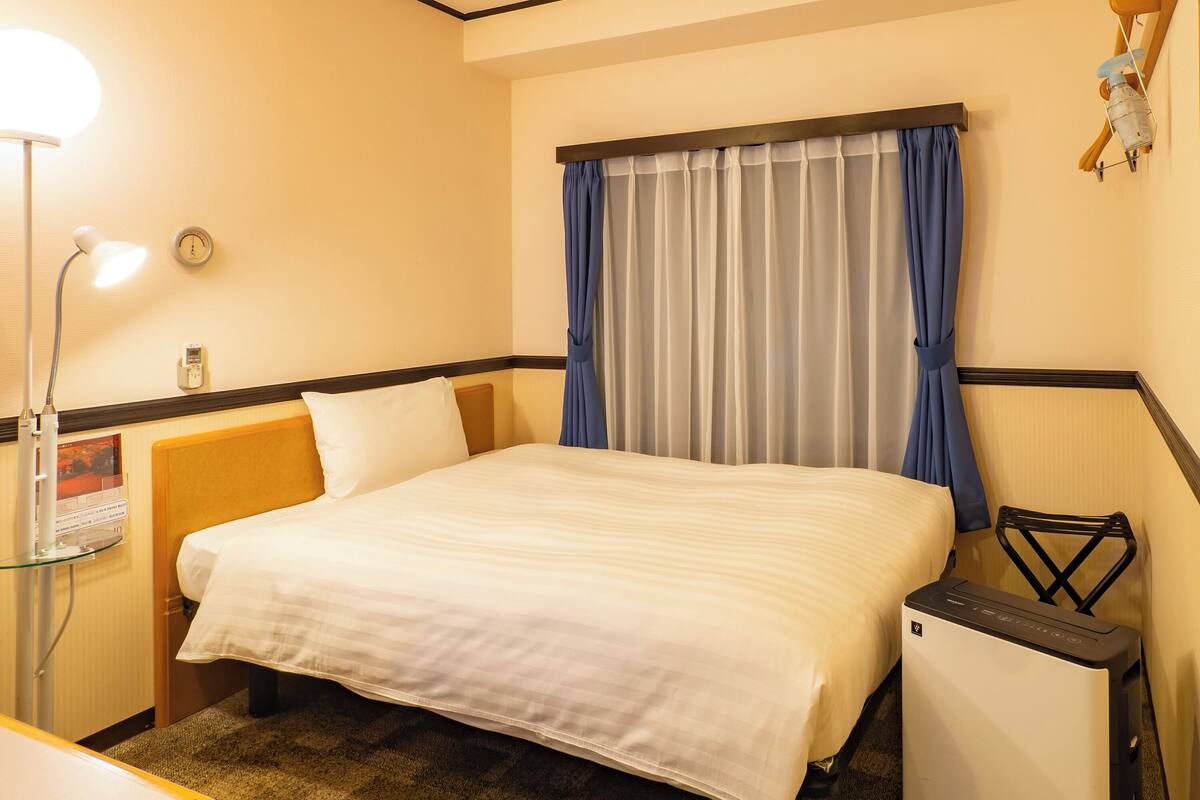 Een hotelkamer met een bed, een bureau, een lamp, een klok en een kleine verwarming.