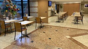 Un restaurante con varias mesas y sillas, un amplio ventanal con vistas, y suelo de baldosas.
