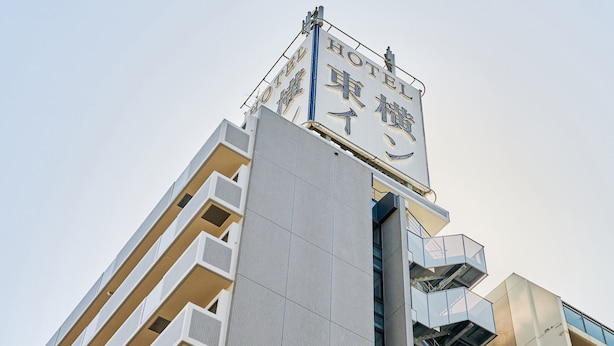 Un moderno edificio de hotel con un cartel llamativo en inglés y otro idioma, que presenta una fachada geométrica y varios balcones.