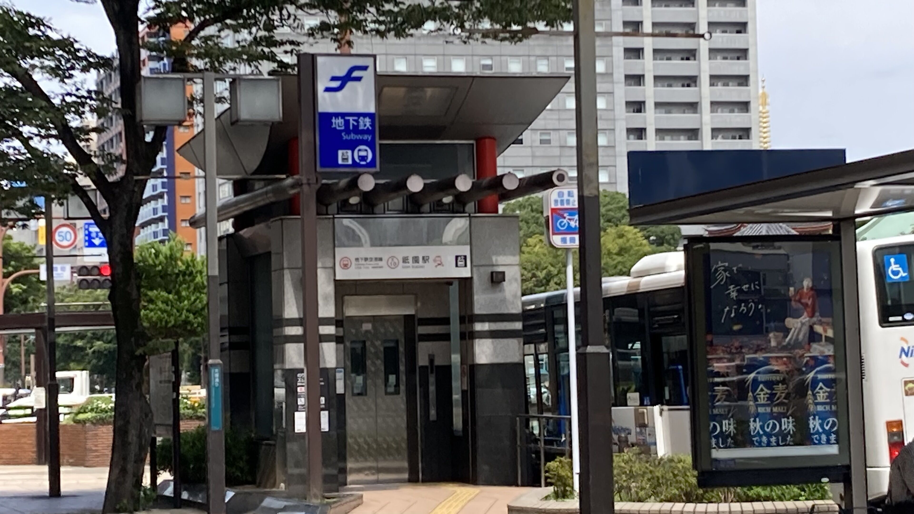 A subway station entrance with a sign indicating a subway entrance, a bus stop with a wheelchair accessibility sign, and a bus with advertisements visible through the window.
