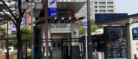 A subway station entrance with a sign indicating a subway entrance, a bus stop with a wheelchair accessibility sign, and a bus with advertisements visible through the window.