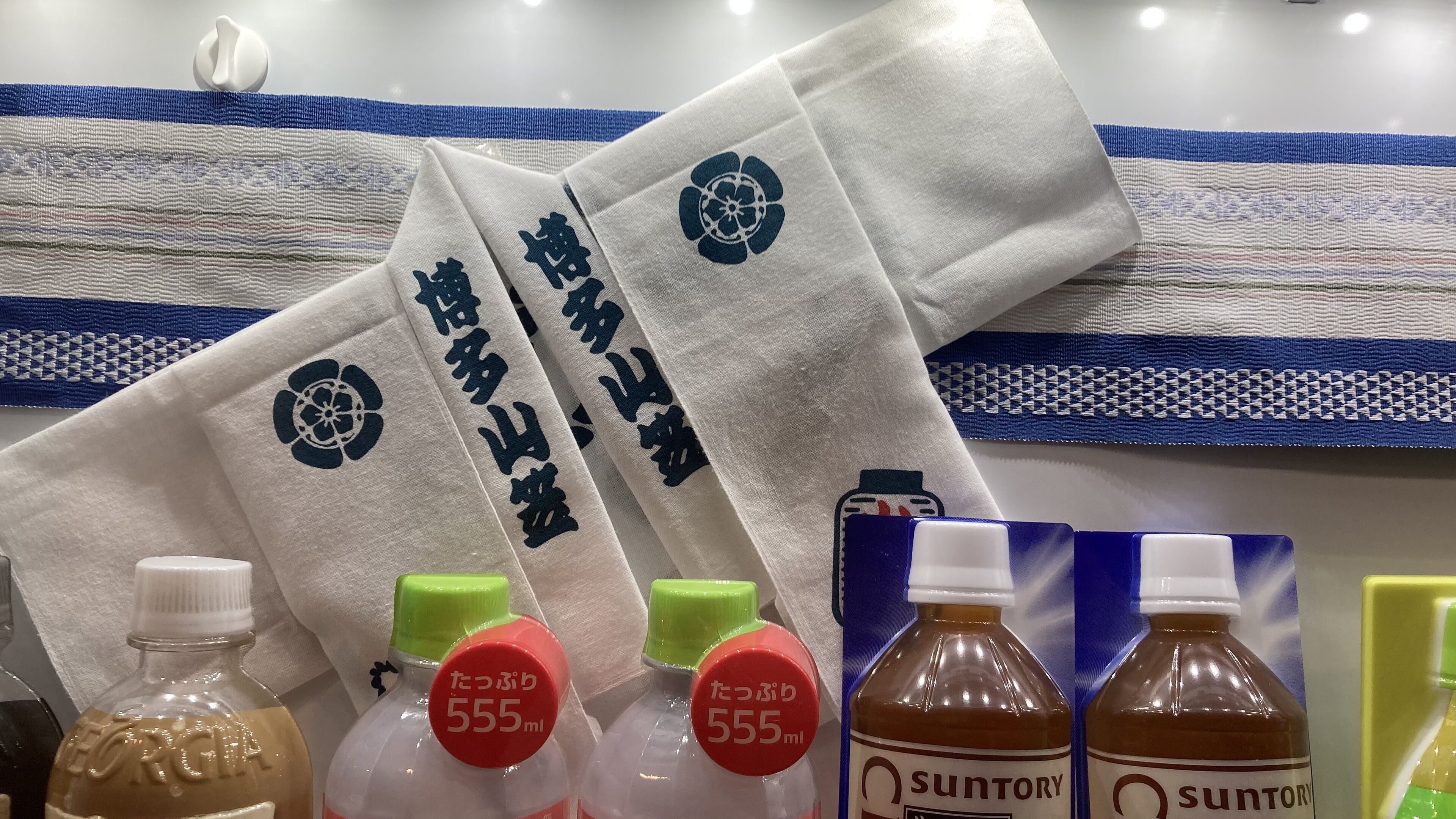 A display of towels with Japanese writing, and bottles of Suntory beverages.