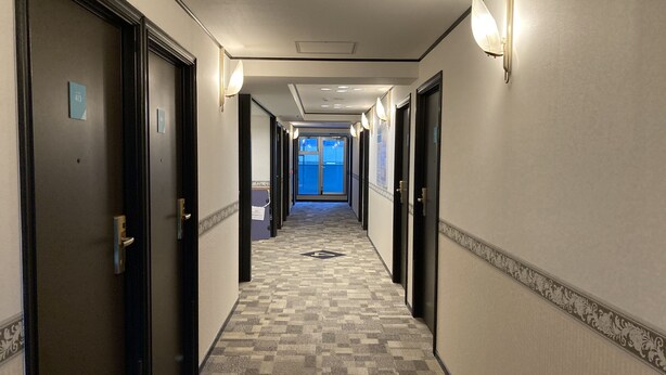 A hotel hallway with carpeted floors, doors on both sides, and wall-mounted lights. - Toyoko Inn Hakata Ekimae Gion (Fukuoka)