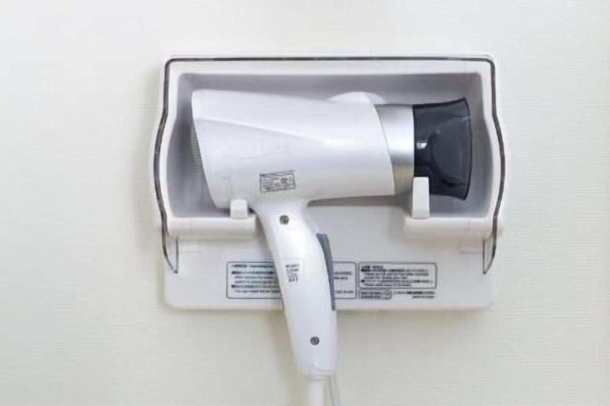 Een haardroger bevestigd aan de muur, met een stekker, bedieningspaneel en een veiligheidswaarschuwing.