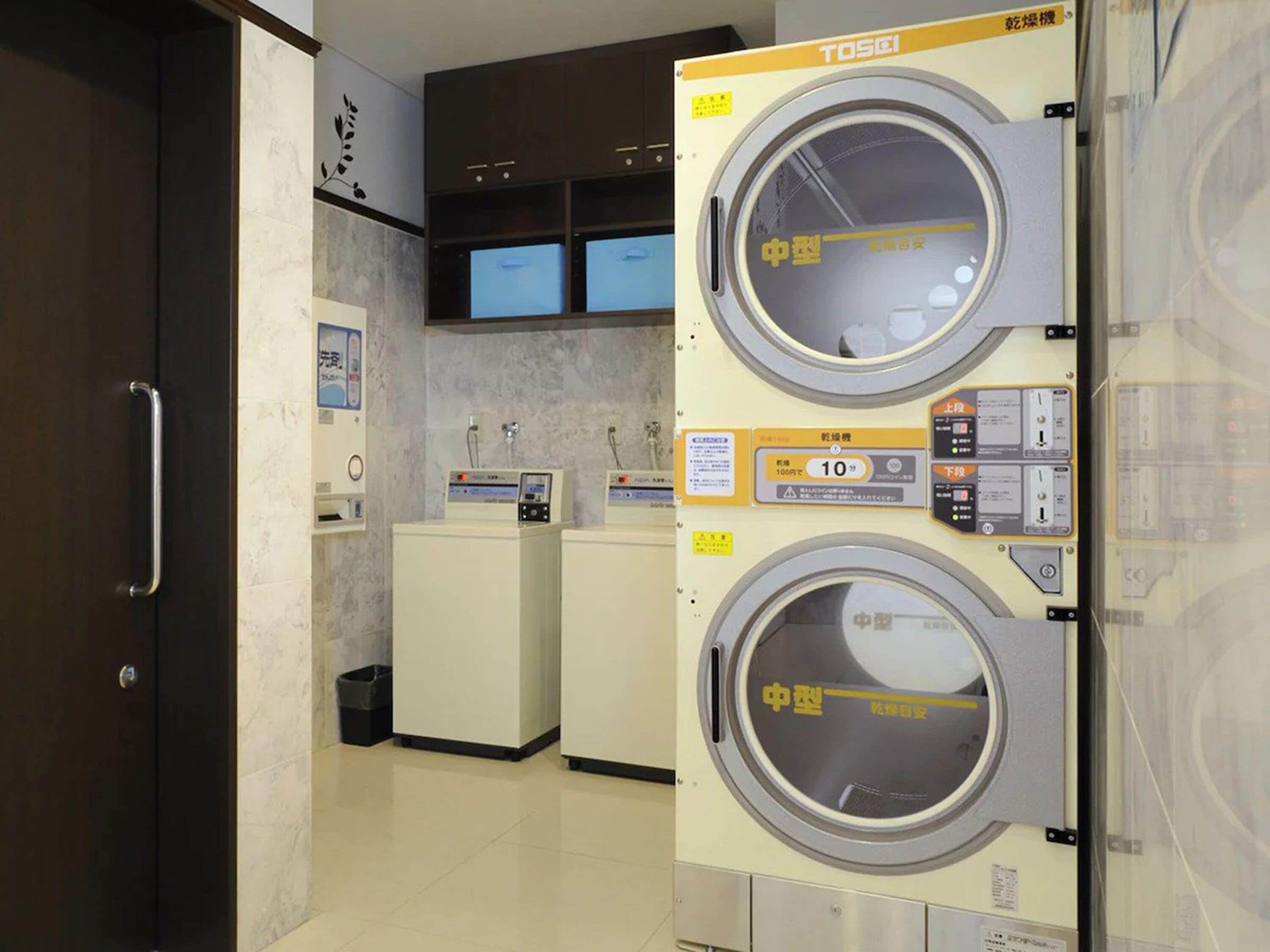 Une buanderie équipée de deux machines à laver superposées, d’un petit évier et d’un meuble avec un miroir.