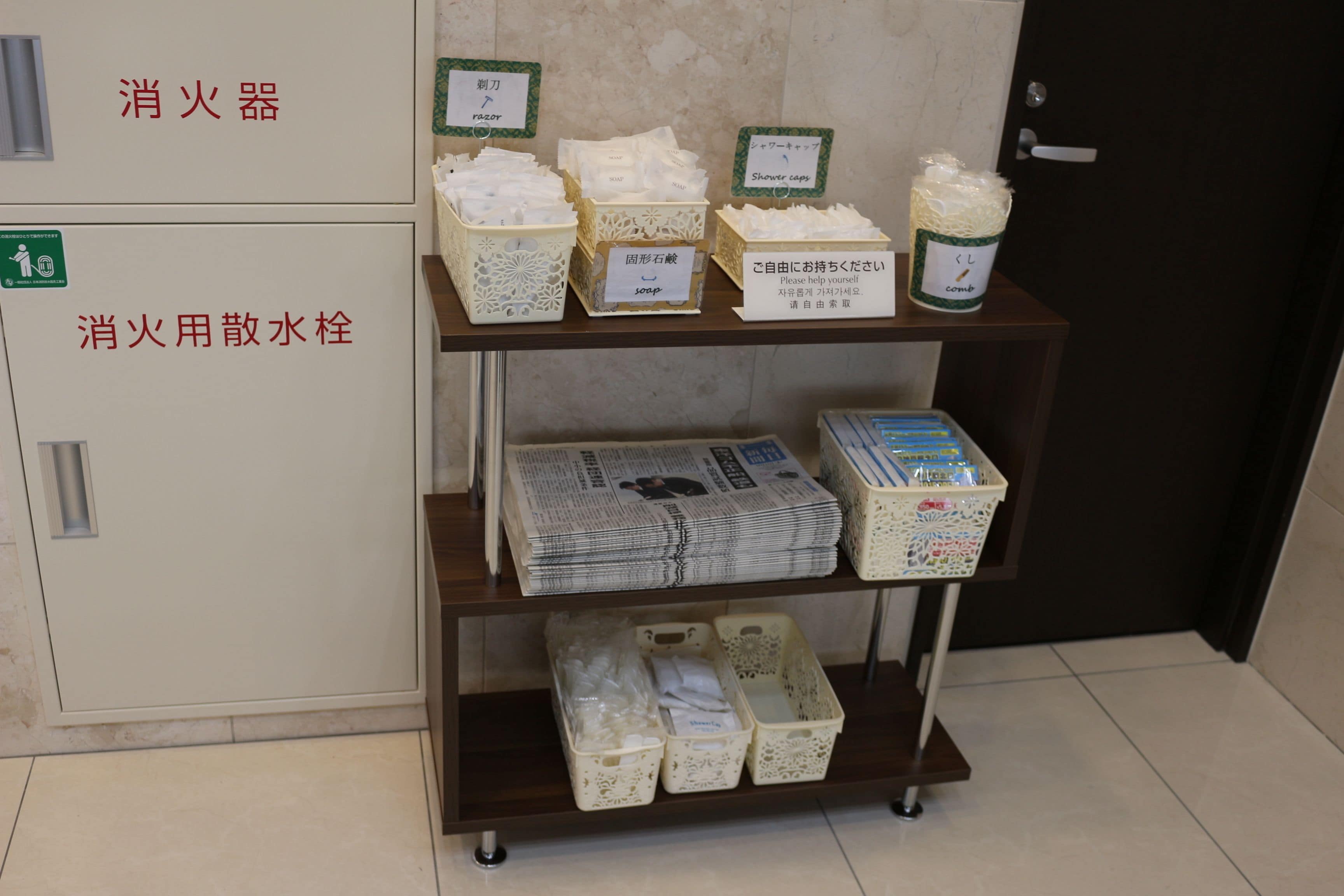 A shelf with various toiletries and supplies, including a fire extinguisher, a first aid kit, and a container of shower caps.