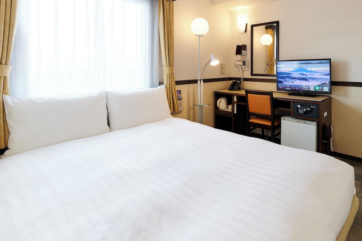 A hotel room with a large bed, a desk with a computer, a television, and a small refrigerator.