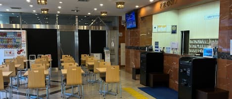 A hotel lobby with a reception desk, seating area, vending machine, and a television screen.