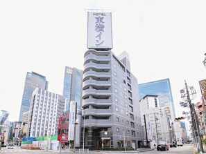 Um hotel moderno com uma placa grande em língua estrangeira, rodeado por edifícios altos em um ambiente urbano.