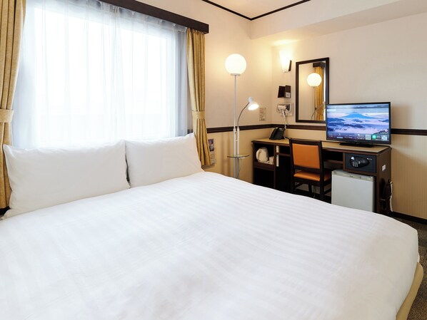 A hotel room with a large bed, a desk with a computer, a television, and a small refrigerator.