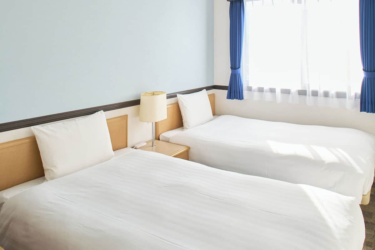 Una habitación de hotel con dos camas, una mesita de noche con lámpara y una ventana con cortinas.