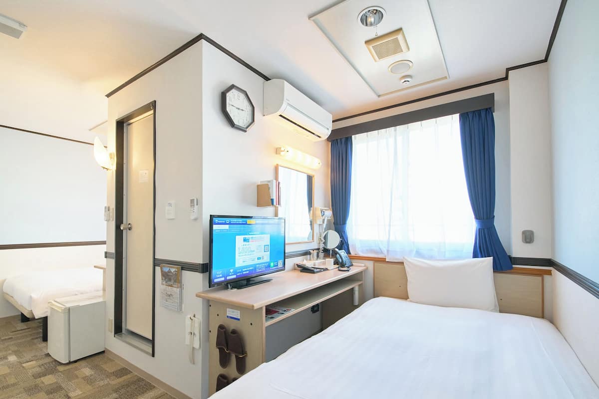 Una habitación de hotel con una cama, un escritorio con computadora, un reloj y una ventana con cortinas.