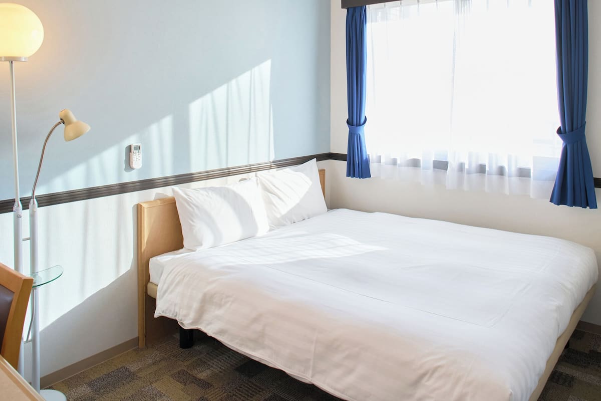 Una habitación de hotel con una cama, un escritorio con lámpara y una ventana con cortinas.