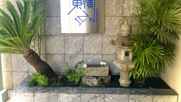 A stone wall with a sign for a hotel, surrounded by potted plants and a stone fountain. - Toyoko Inn Kyoto Shijo-omiya (Kyoto)