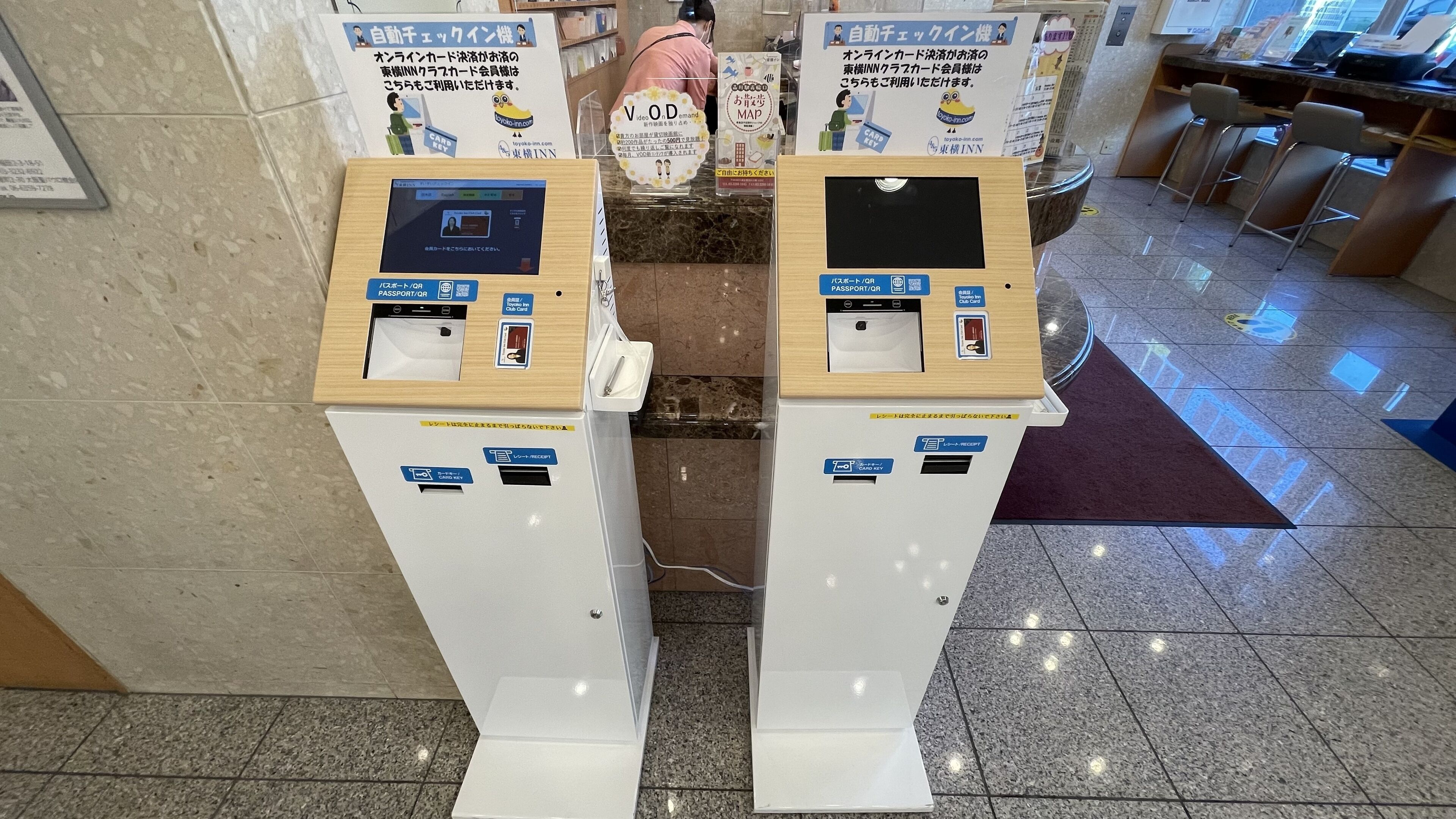 Zwei Automaten für Kartenabwicklung mit Anweisungen auf Japanisch, ein Schalter mit Angestelltem sowie eine Sitzgelegenheit mit Stühlen.