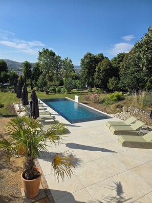 A rectangular pool with clear blue water, surrounded by a tiled deck. There are lounge chairs and umbrellas along the poolside. - Eclosion Château Hôtel & Restaurant (Saint-Paul en Jarez)