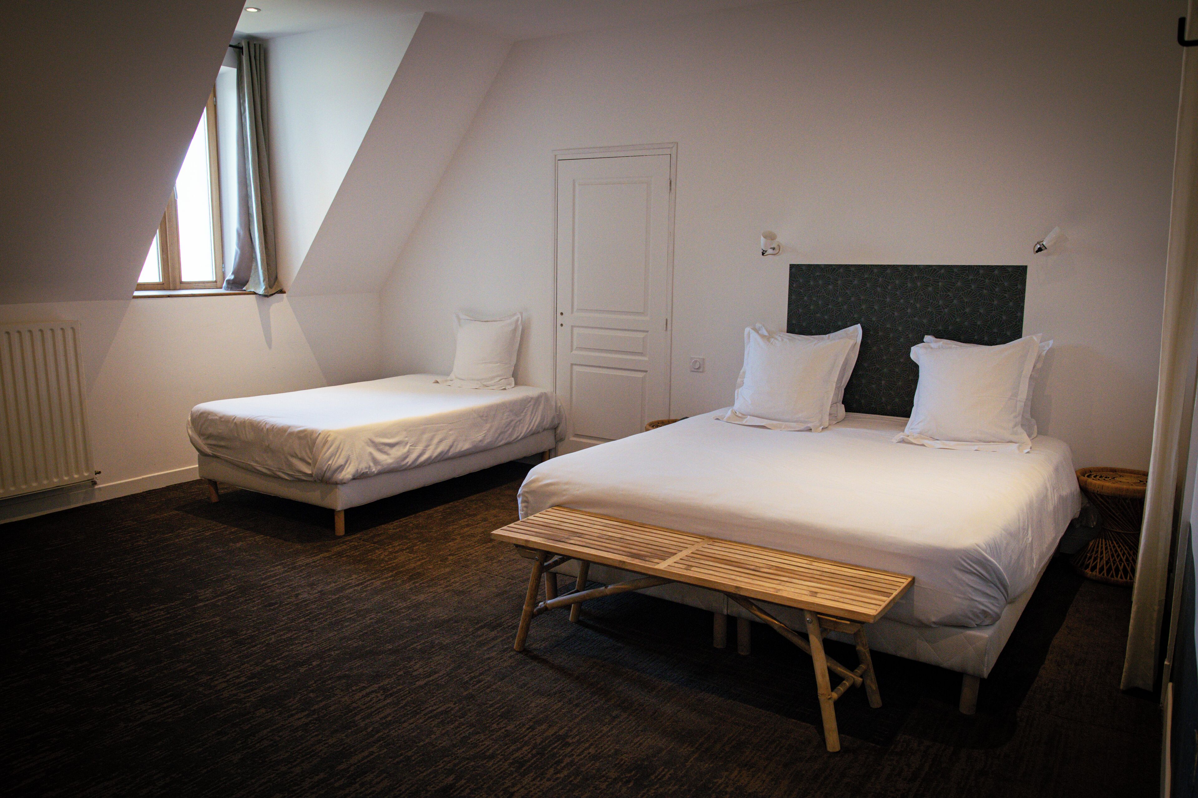A room with two beds, a window, a radiator, and a wooden bench.
