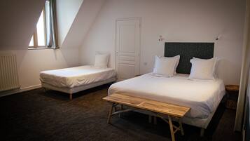 A room with two beds, a window, a radiator, and a wooden bench.