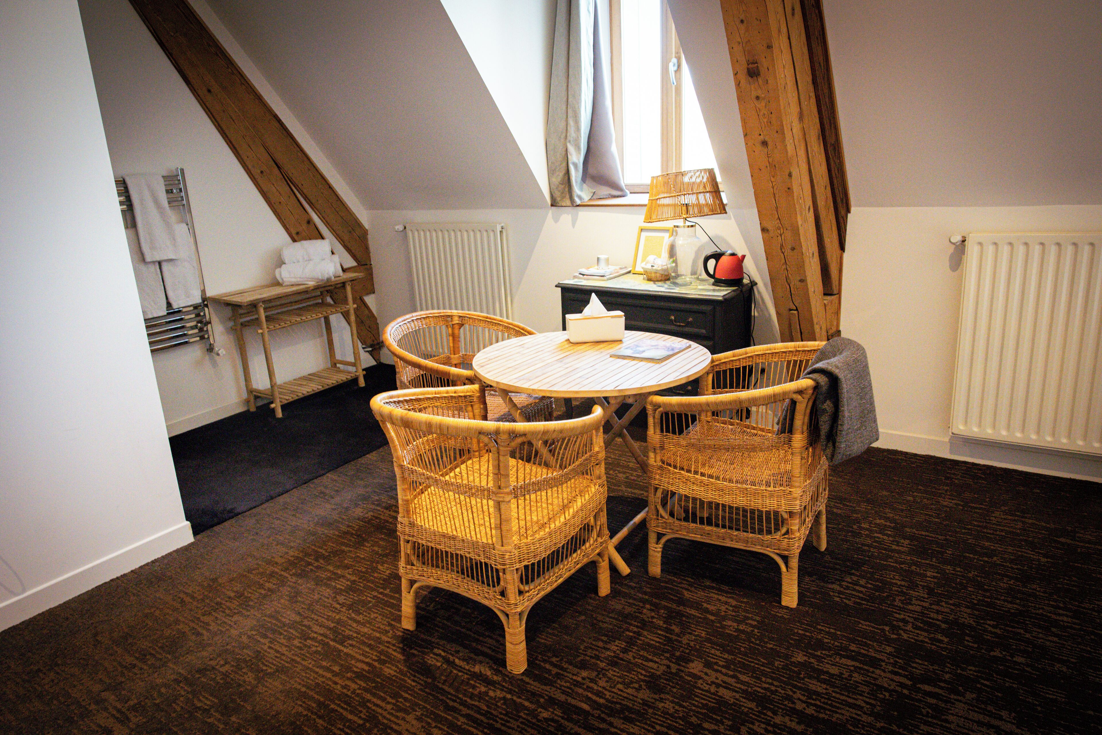 A cozy room with a round table and four wicker chairs, a radiator, and a window with curtains.