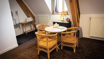 A cozy room with a round table and four wicker chairs, a radiator, and a window with curtains.