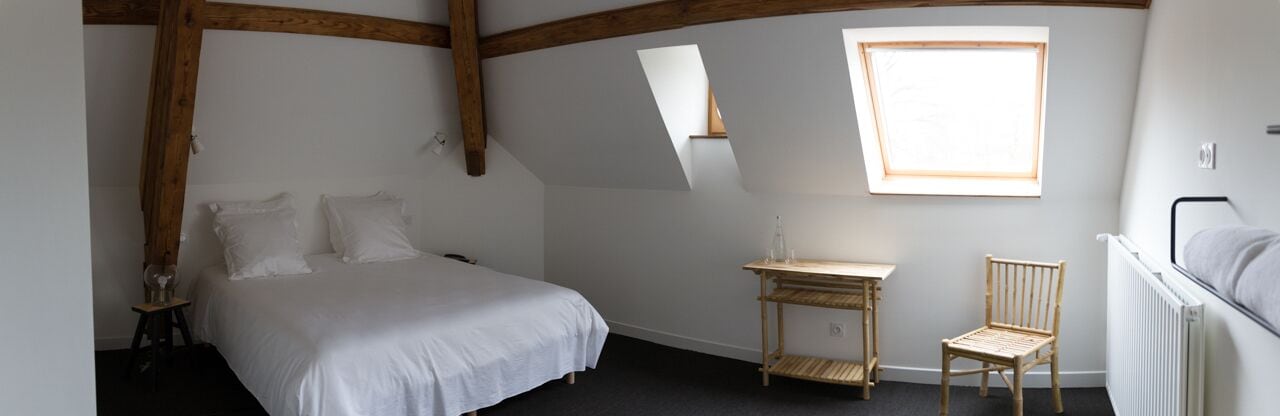 A bedroom with a bed, a small wooden table, a chair, and a window.