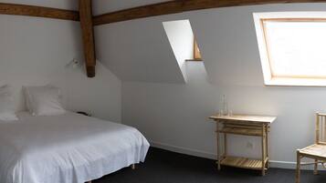A bedroom with a bed, a small wooden table, a chair, and a window.