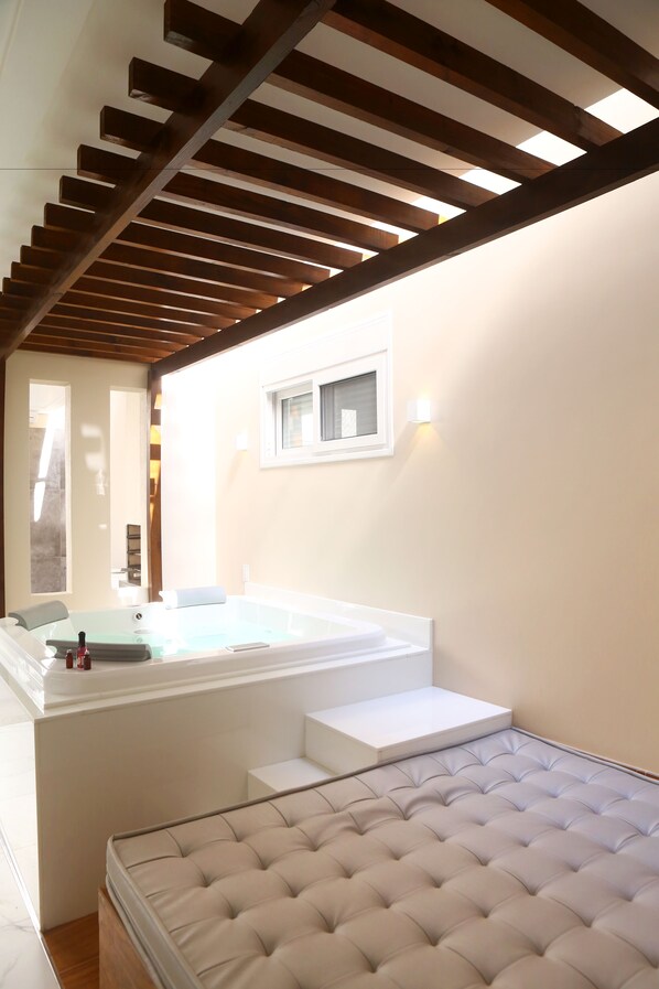 Un dormitorio moderno con una cama grande, un jacuzzi integrado y una estructura de techo de madera.