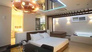 A modern hotel room with a large bed, a desk with a chair, a glass partition, a bathtub, and a ceiling light fixture. - Zaya Motel Premium - Adults Only (Florianópolis)