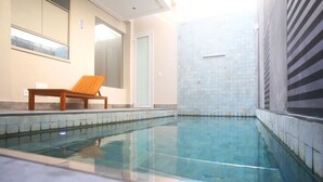 A swimming pool with a wooden chair, tiled walls, and a door. - Zaya Motel Premium - Adults Only (Florianópolis)