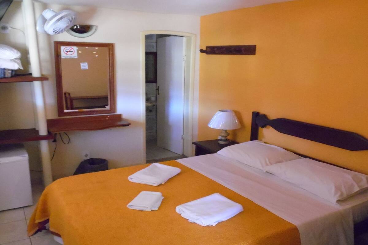 A hotel room with a bed, a nightstand with a lamp, a mirror, and a towel rack.