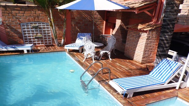 Un espace piscine agrémenté de chaises longues rayées de bleu et de blanc, d’une terrasse en bois et d’un mur en briques.