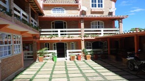 Un bâtiment à deux étages, doté d’un toit en tuiles, de plusieurs balcons et d’un patio couvert agrémenté de plantes en pot.