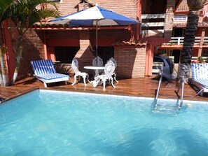 A swimming pool with lounge chairs and a table, surrounded by a brick patio and palm trees. - Pousada Brilho Da Serra (Tiradentes)